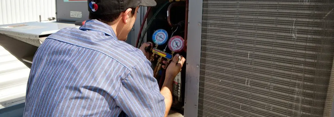 HVAC technician servicing a condenser unit in Ash
